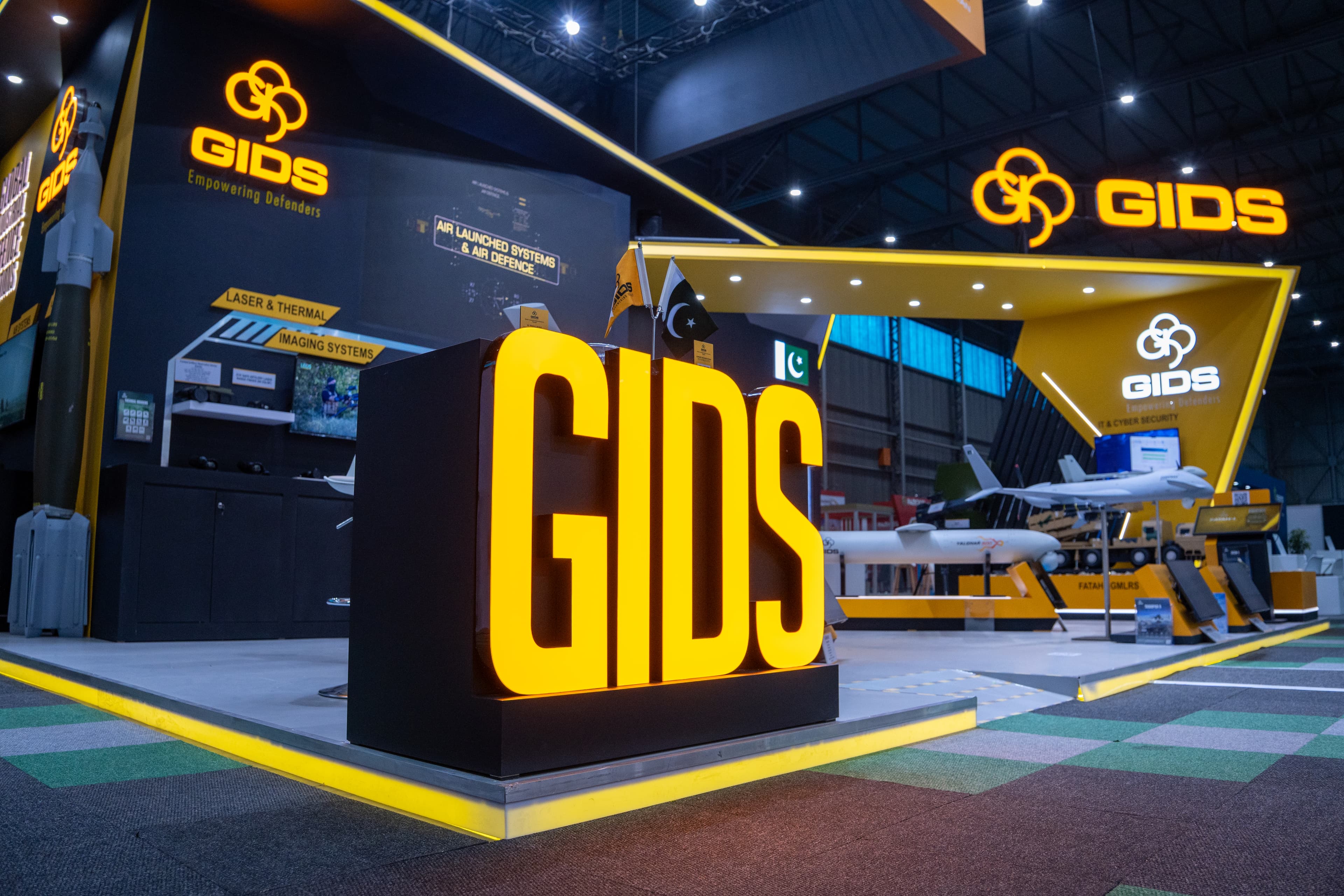 Large illuminated GIDS sign at a yellow and black exhibition booth showcasing military defense equipment.