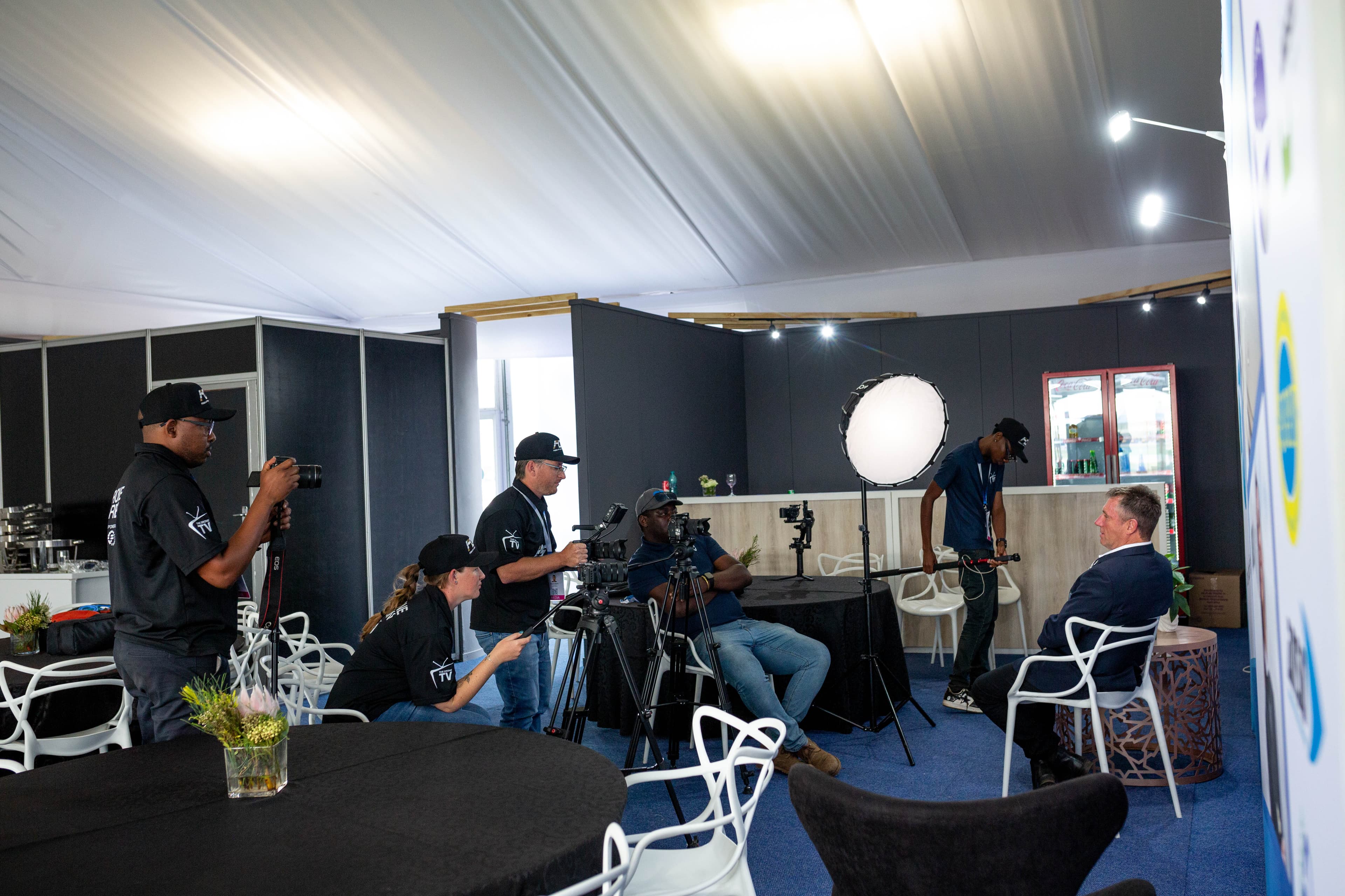Media crew filming an interview with a man in a suit inside an event tent.